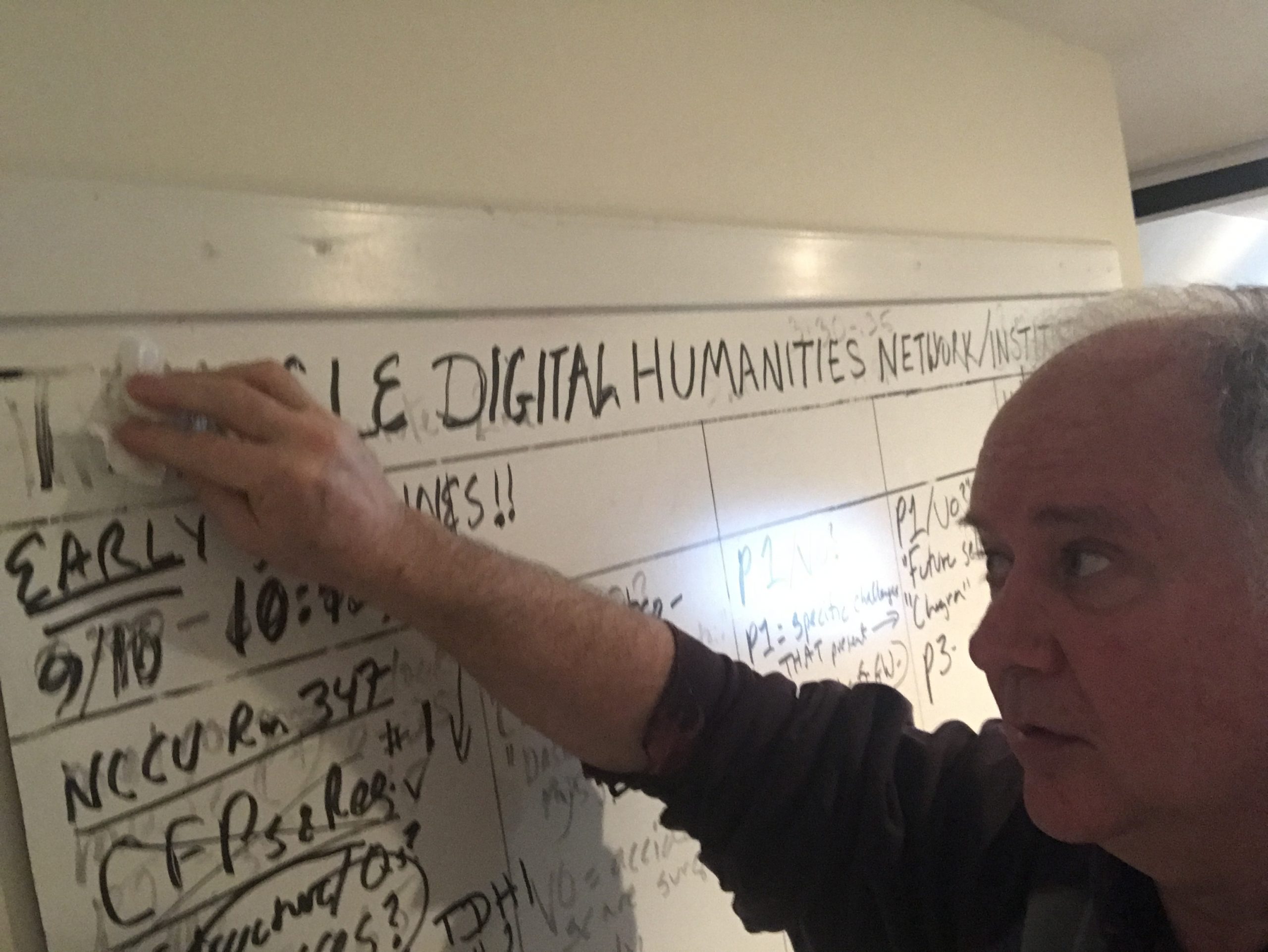 A middle-aged white man erasing a white board full of a semester's work.